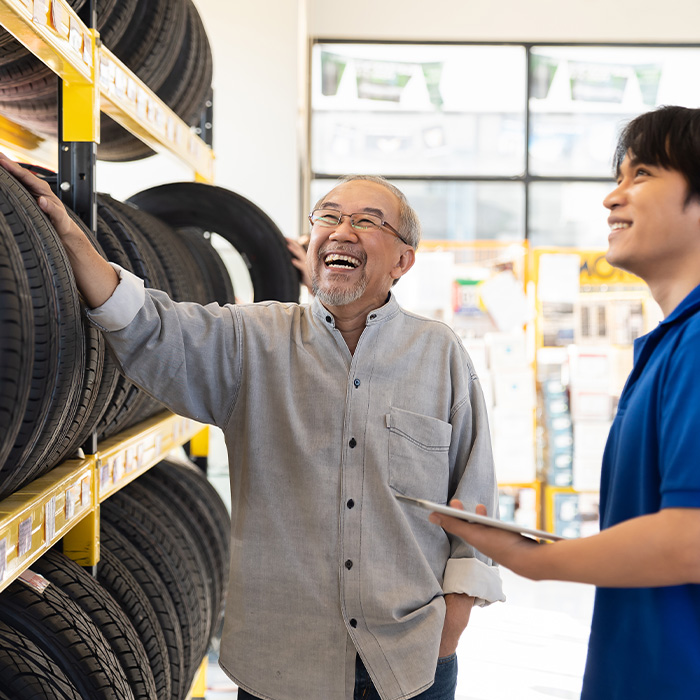 Asian salesman recommend new tire wheel on shelves shelf to senior elderly customer at the auto car repair shop