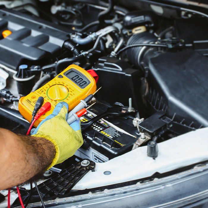 A mechanic holds a digital multimeter to check the car electrical system