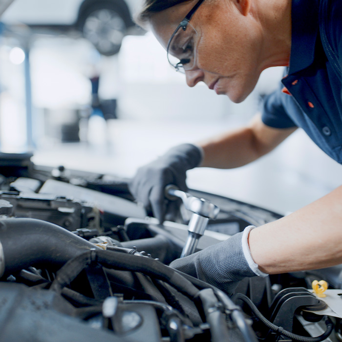 Female Mechanic With Socket Wrench Working On Car Engine In Auto Repair Shop