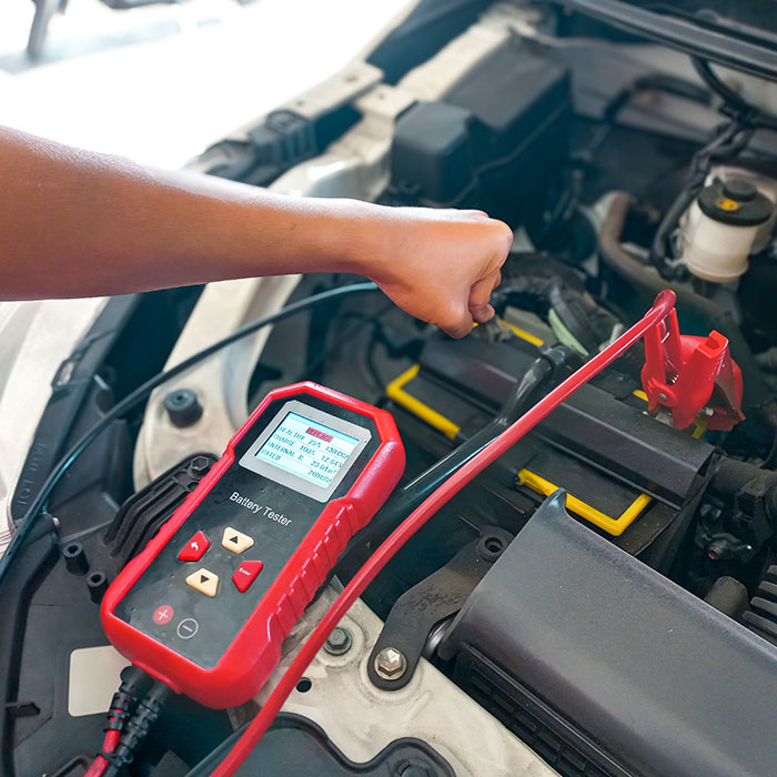 Car mechanic repairer checking and testing automotive accumulator with digital electronic battery tester