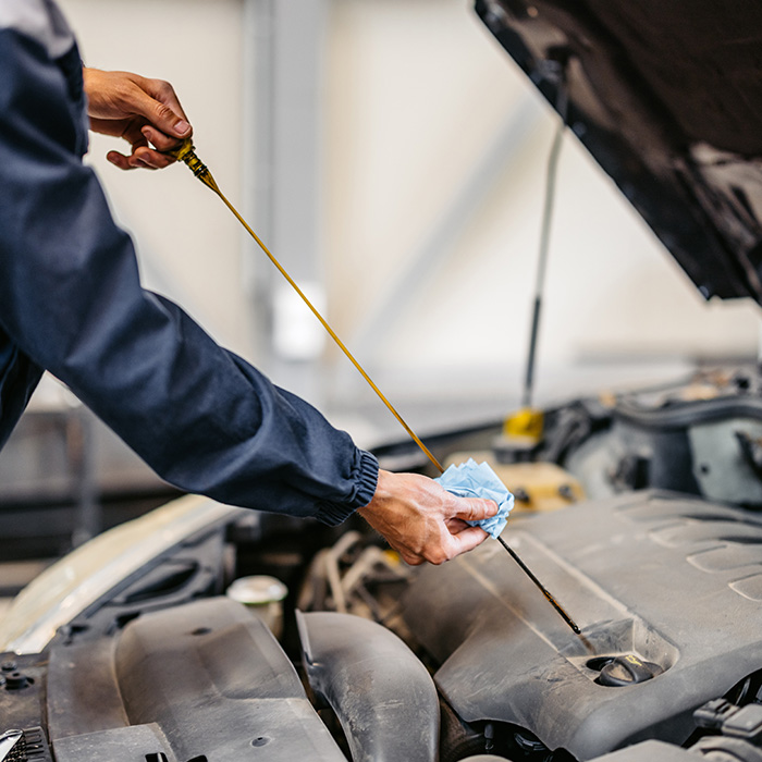 Young male car mechanic checking an engine oil on a car he is working on in his garage