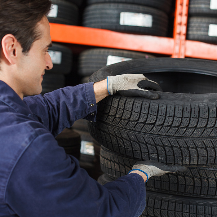 Mechanic lifting new car tire from stack of tires inventory to make a vehicle repair in an auto garage