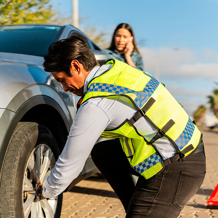 Car insurance agent changing customer's flat tire at road