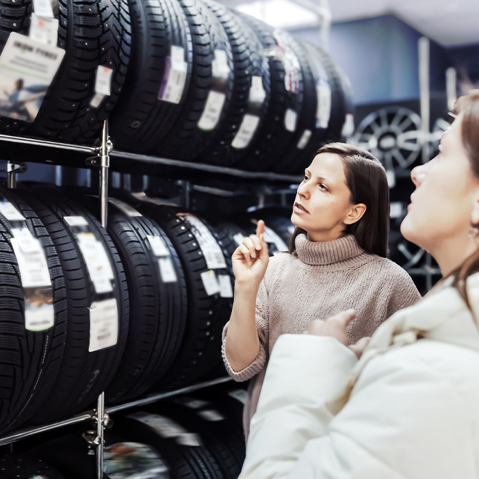 One woman thoughtfully examines available tires displayed on shelves while seller provides guidance