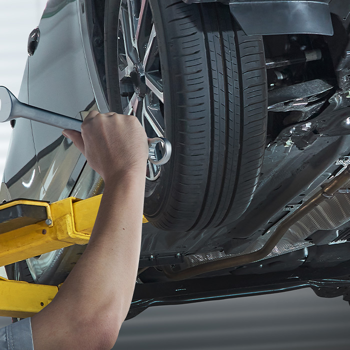 Mechanic tightening a car wheel using a wrench while the vehicle is raised on a hydraulic lift inside an auto repair shop