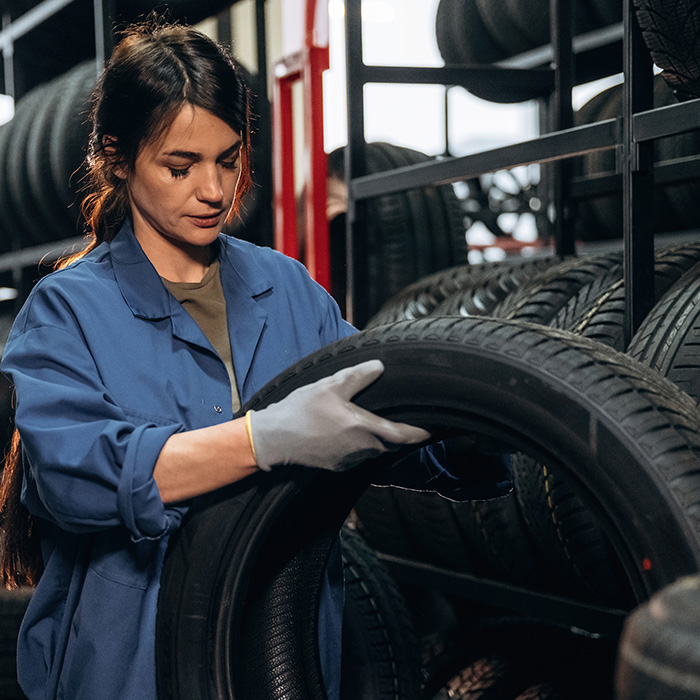 Woman in blue coveralls examines a tire in a tire shop
