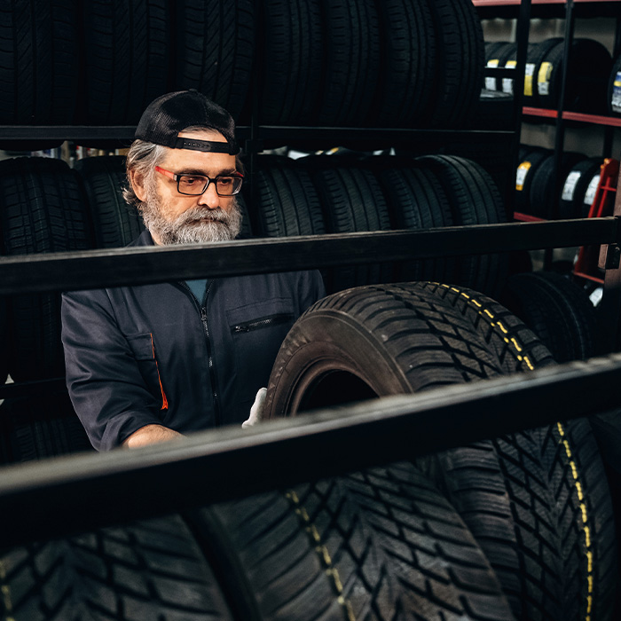 Male tire technician wearing glasses inspects tires on a rack in an automotive shop